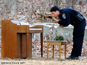 A police officer examines an oddly placed piano in the woods of Harwich, Massachusetts.