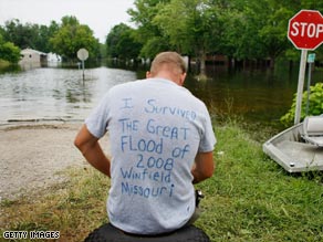 James Burt sits on an embankment near a neighborhood inundated with floodwaters in Winfield, Missouri.