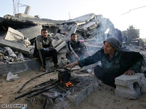 A Palestinian woman makes tea on a wood fire as she sits with her sons amid the rubble of houses in Gaza.