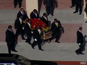 Seven men wheel out a golden casket covered in red flowers from Forest Lawn's Hall of Liberty.