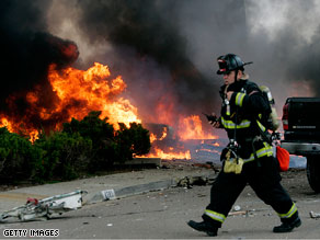 A firefighter walks past as flames rise from the wreckage of a military jet crash in California.