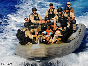 Members of the U.S. Navy take a young Somali boy to safety after rescuing him and 51 others adrift in a skiff.