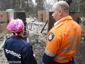 A policeman and forensics officer look over a house where five people died at Kinglake, north of Melbourne.