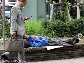 A businessman walks past a homeless man taking a nap at a Tokyo park.