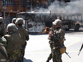 Thai troops pass a smoldering bus during unrest this week in central Bangkok.