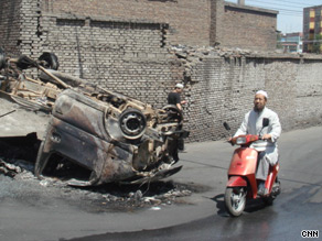 A Muslim motorcyclist drives by a charred car in Urumqi. July 9, 2009.