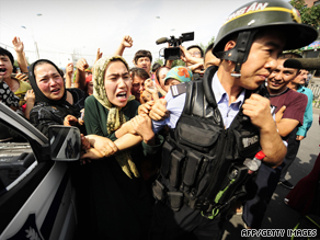 Ethnic Uyghur women grab the arm of a policeman as they protest in Urumqi on July 7.