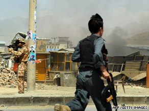 An Afghan police officer runs toward the scene of a car bomb Tuesday as a NATO soldier aims his weapon.