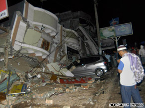 A resident stands next to building that collapsed onto a car in Padang, Indonesia, on Wednesday.