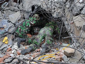 Indonesian soldiers crawl under the rubble of a collapsed building to search for victims.