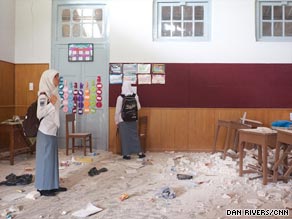 Students inspect their damaged classroom, with tables broken and shards littering the ground.