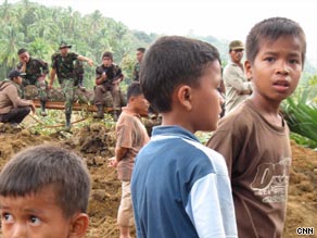 Children stand near to soldiers helping with the recovery of bodies in the village.