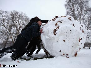 A group of men push a giant snowball across Kensington Gardens, west London.