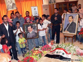 An Iraqi poet, left, gives a recital while children carry pictures of Saddam Hussein over his grave.