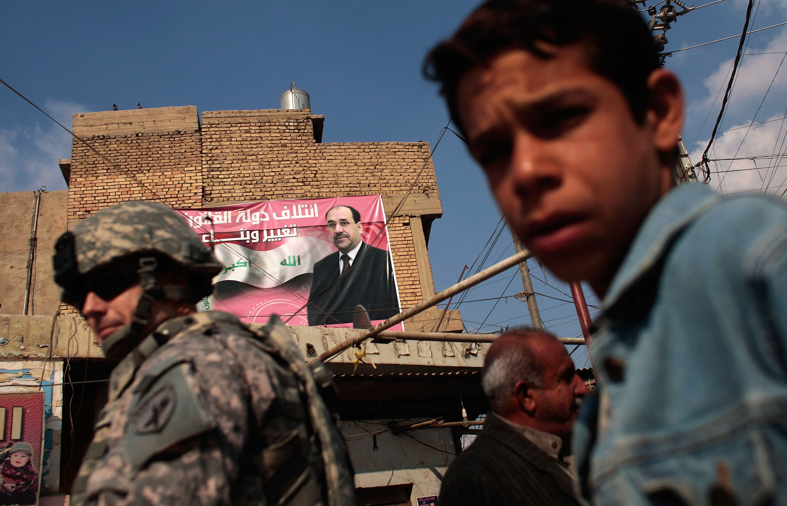 Chris Hondros/Getty Images. A boy and a soldier in the U.S. Army's 172nd Brigade Combat Team stand near a campaign poster touting Iraqi Prime Minister Nouri al-Maliki in Musayyib, in the Babil Province, Iraq.