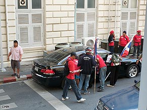 Red-shirted protesters surround a car in a residential street in Bangkok.