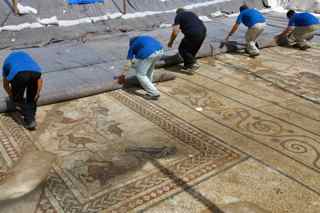 David Silverman/Getty Images. Workers remove the cover from an ancient Roman mosaic as it is revealed some 13 years after it was first discovered in the ruins of a 4th century AD building, on July 1, 2009 in Lod in central Israel. The beautiful 1,700 year old mosaic floor, which is regarded as one of the most magnificent and largest ever revealed in Israel, was first uncovered in 1996 during a project to upgrade the city's sewage system. The well-preserved mosaic covers an area of about 180 square meters and is composed of coloured carpets that depict in detail animals, birds, fish, a variety of flora and the sailing and merchant ships that were used at the time.
