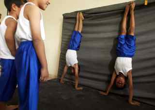MOHAMMED SAWAF/AFP/Getty Images. Iraqi children perform hand-stands at a gymnasium on the outskirts of the southern city of Karbala, some 110 kms from Baghdad, on July 12, 2009. The club, which is popular during the summer school holidays, is frequented by boys and girls, providing gymnastic lessons to children and teenagers up to the ages of 19-years-old.