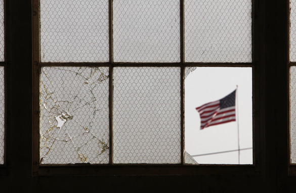 In this photo, reviewed by the US military, an American flag waves, pictured through a broken window from inside a vacant airplane hangar used for media activities at Camp Justice, site of the US war crimes tribunal compound at Guantanamo Bay US Naval Base, Cuba, Thursday, July 16, 2009. (AFP/Getty Images)