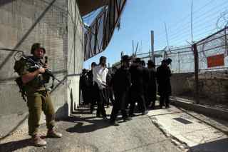 MENAHEM KAHANA/AFP/Getty Images. An Israeli soldier stands guard as ultra-Orthodox Jews visit the site which they believe to be Rabbi Ashi's tomb, divided by a border electric fence, along northern Israel's border with Lebanon near Kibbutz Manara on August 4, 2009.
