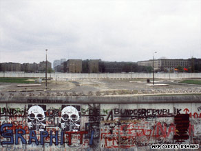 Graffiti is painted on Berlin Wall on West Berlin side while East German and Soviet flags fly on the other side of the East Berlin no-mans-land spiked with anti-tanks traps.