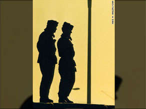 Two East German border guards atop the Berlin Wall look westward