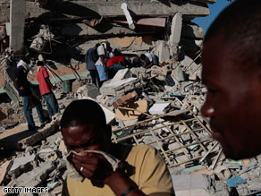 Haitians pass in front of the multi-story St. Gerard School that collapsed, leaving what is feared to be dozens trapped or killed under the rubble in Port-au-Prince.