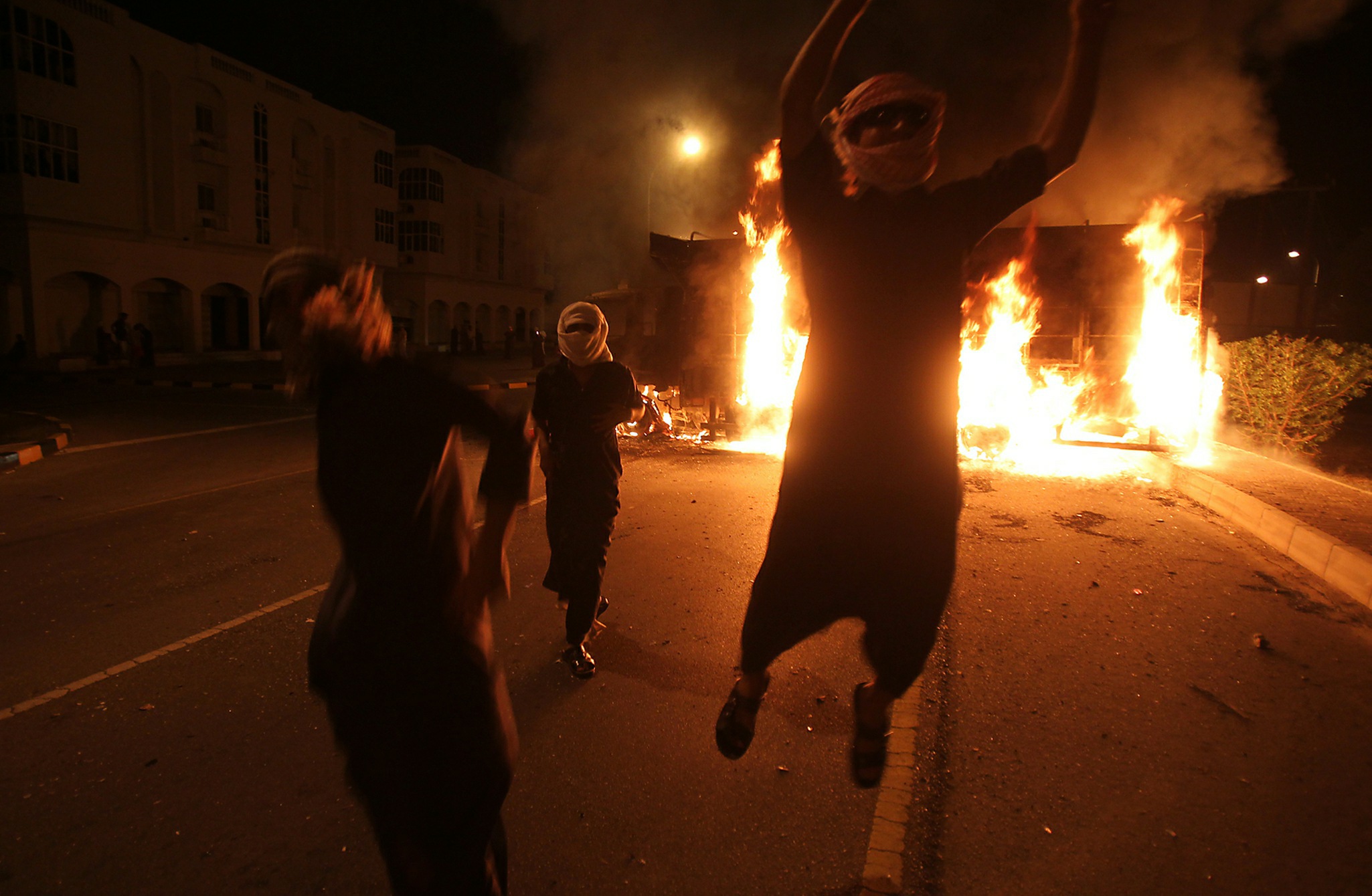 Masked Omani protesters jump in front of burning vehicles during a demonstration in Sohar, more than 200 kms (125 miles) northwest of Muscat. Getty Images/AFP.