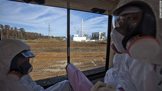 People wearing protective suits and masks ride on a bus past the crippled Fukushima Daiichi nuclear power station in Okuma, Japan, on Saturday, November 12. Journalists got their first ground-level glance around the stricken facility, eying shells of reactor buildings, tons of contaminated water, and workers still scurrying to mitigate damage from a crisis that began eight months ago.