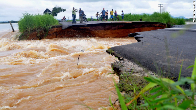 People watch water run through a washed-out road Thursday in Brazil's Rio de Janeiro state.