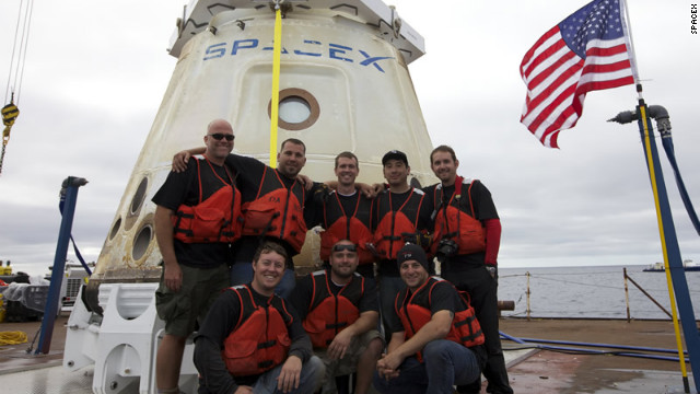 Dragon's recovery team poses in front of the first commercial capsule to reach orbit and return safely to Earth.