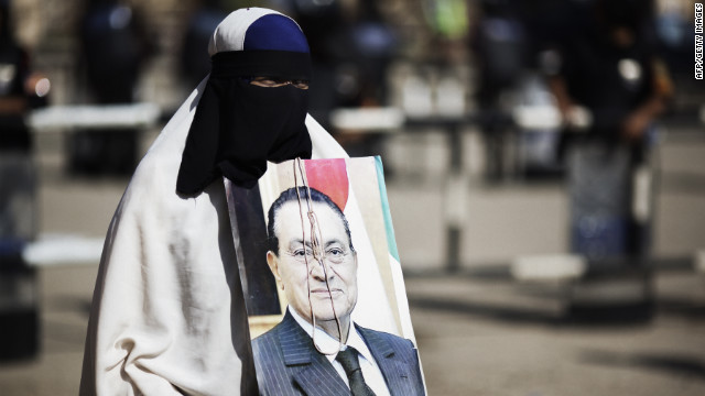 A fully veiled Muslim Egyptian woman holds a portrait of Mubarak outside of the courthouse in Cairo. The image is adorned with a hangman's noose.