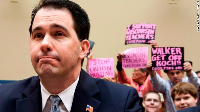 Walker testifies at a House Oversight and Government Reform Committee hearing on Capitol Hill in Washington as protesters wave signs behind him, April 14, 2011. 