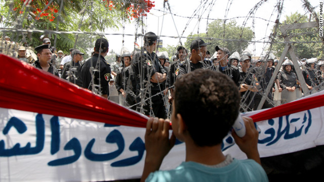 A boy peers through barbed wire at Egyptian military police standing guard outside the Constitutional Court in Cairo on Thursday, June 14.