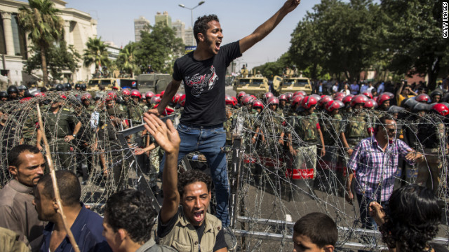 A protester stands on a barricade of barbed wire as Egyptian military police stand guard. Egypt's Supreme Constitutional Court ruled that the Islamist-led parliament must be immediately dissolved.