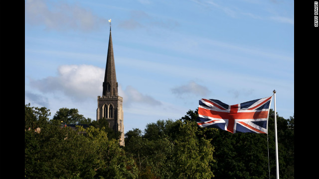 A Union Jack flaps in the breeze outside the All-England Club with the spire of St. Mary's Church in the background.