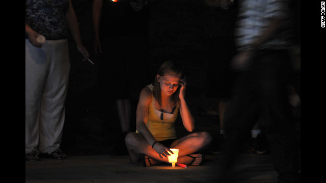 A woman holds a lit candle at a makeshift memorial.