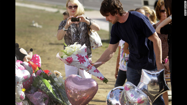 Bale places flowers at the memorial while other mourners look on.