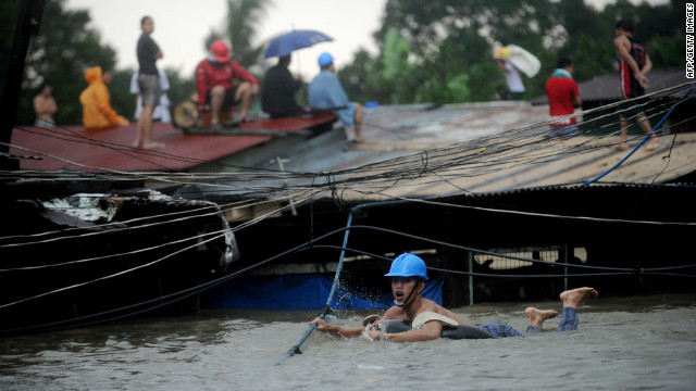 A man tries to cross floodwaters by following a robe as other residents wait on their roofs in Manila. At least five people were killed and seven were missing as torrential rains brought the Philippine capital to a standstill, with floodwaters covering half the sprawling city, officials said.