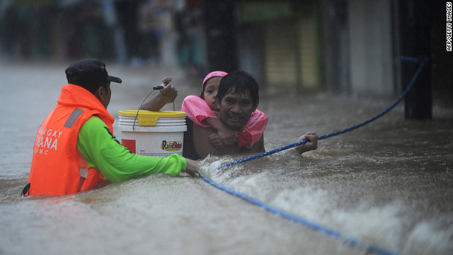 A rescuer guides a father carrying his daughter on his back through a strong current.