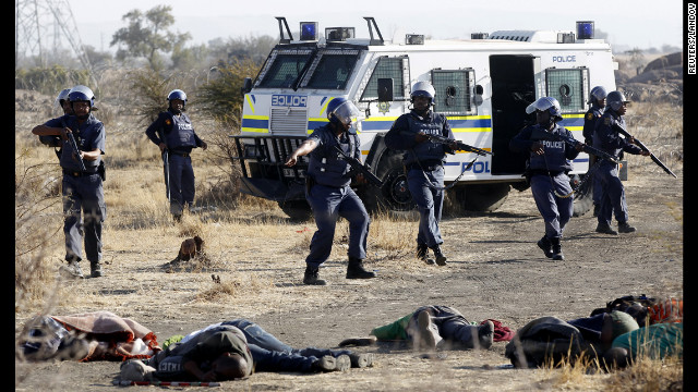 A policeman gestures in front of some of the miners after they were shot. Police have not released a death toll, but a South African Press Association reporter counted 18 corpses. It is feared more could be dead.