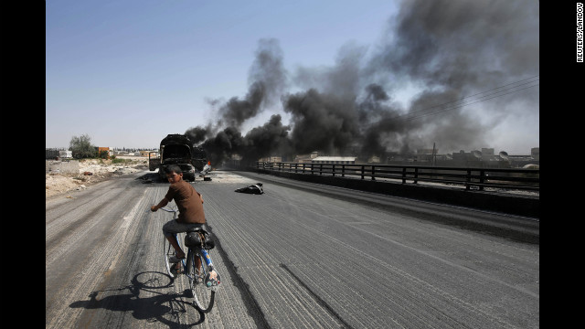 A boy rides a bicycle toward fuel trucks struck by missiles from fighter jets in the Bab al-Nayrab district of Aleppo, Syria, on Monday, August 27. 