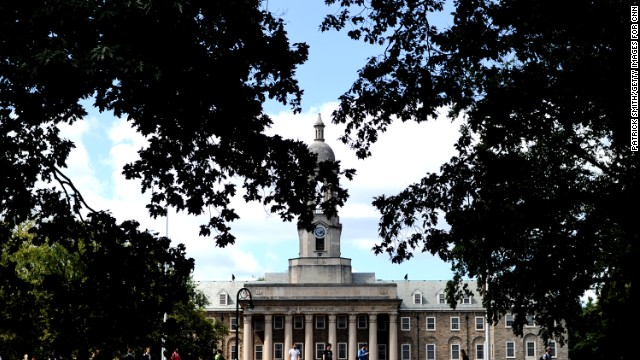 The clock tower of the Old Main building peeks through the trees on campus.