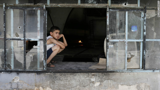 A boy sits at a window spotted with bullet holes at a local bakery.