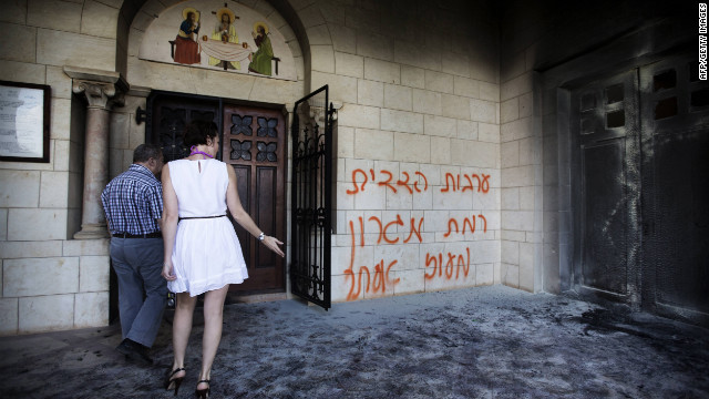 Tourists look at a burnt door as they walk past grafitti sprayed on the wall of the Christian Catholic Latrun monastery on Tuesday.