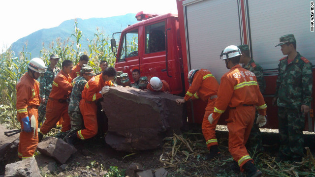 Rescuers remove a rock from a road in Yiliang.