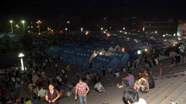 Residents rest by the makeshift tents (back) at an emergency relief center set up in the town square in Yiliang.