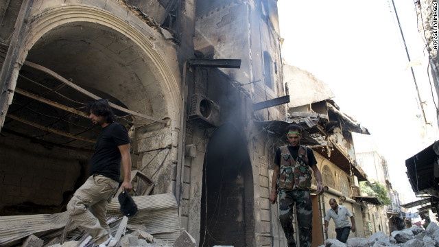 Fighters and civilians walk past buildings damaged during fighting between rebel and government forces in Aleppo on Thursday.