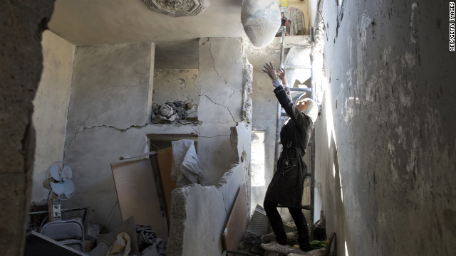 A Syrian woman prepares to grab a bag of belongings as she stands amid rubble at a house where a child was killed Friday.