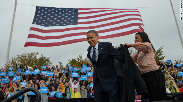 Barack Obama is assisted with putting on a raincoat onstage during a campaign rally at Cleveland State University on Friday.